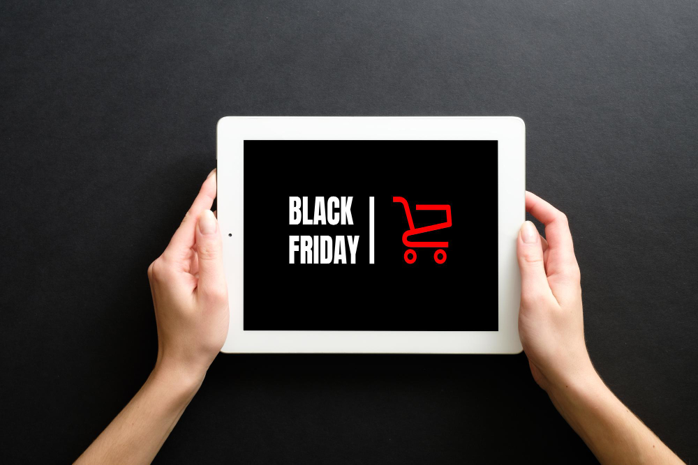 Imagem ilustrativa de um tablet, com a figura de um carrinho de compras, e uma pessoa apontando para ele, representando a black friday.